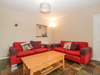 A living room with two red sofas with animal and plaid cushions a wooden coffee table and a floor lamp at Pippins in Bream
