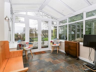 A conservatory with two patterned chairs a wooden bench a table against the wall a standing lamp and a television on a stand at Pippins in Bream