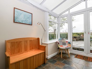 A conservatory with a wooden bench a standing lamp a patchwork chair and glass doors opening to a garden at Pippins in Bream