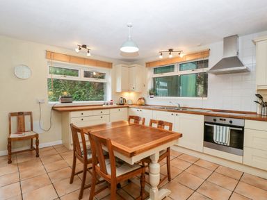 A kitchen with a wooden dining table and four chairs a stove with an oven a range hood two windows with blinds and tiled floor at Pippins in Bream