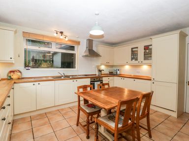 A kitchen with wooden dining table and chairs white cabinets and a window at Pippins in Bream