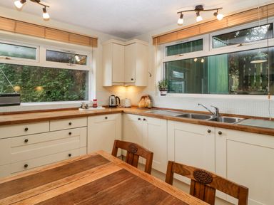 A kitchen with white cabinets wooden countertops a double sink and a wooden dining table with chairs at Pippins in Bream