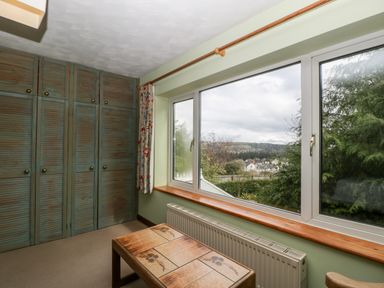 A small room with wooden wardrobe cabinets a radiator under a large window and a wooden coffee table at Pippins in Bream