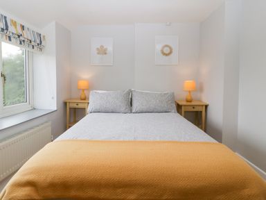 A bedroom with a bed between two bedside tables with lamps and framed pictures above at Pippins in Bream