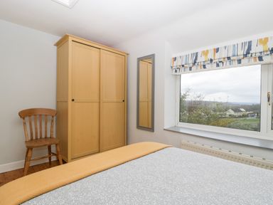 A bedroom with a wooden chair a wardrobe a bed with a gray and white bedspread and an orange blanket and a window with a patterned blind at Pippins in Bream