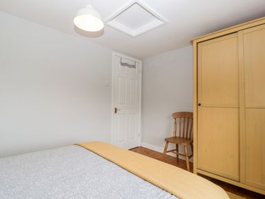 A bedroom with a bed covered in a grey and white patterned duvet and a yellow blanket a wooden chair a yellow wardrobe and a white door at Pippins in Bream
