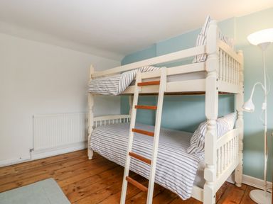 A bedroom with a wooden bunk bed with striped bedding and a floor lamp on a wooden floor at Pippins in Bream