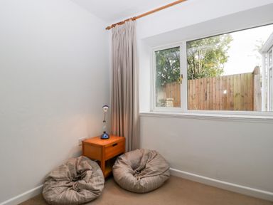 A small room corner with two bean bags a wooden side table with a lamp and a window overlooking a wooden fence at Pippins in Bream