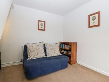 A small room with a blue sofa with bicycle patterned cushions a wooden bookshelf with books and framed pictures on white walls at Pippins in Bream