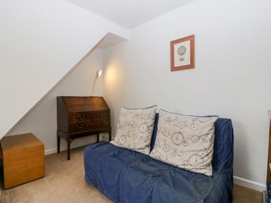 A small room with a blue sofa with bicycle patterned cushions a wooden writing desk with a lamp and a small wooden box at Pippins in Bream