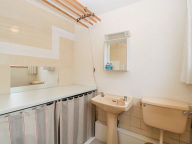 A bathroom with a sink toilet mirror and storage area with curtains at Pippins in Bream