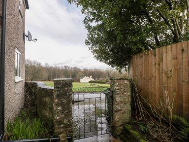 A stone wall with a metal gate next to a house garden and a wooden fence at Pippins in Bream
