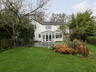 A backyard with green grass, trees, and shrubs in front of a white two-story house with a glass conservatory at Pippins in Bream