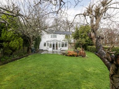 A backyard with grass lawn trees plants and a white two story house with a conservatory at Pippins in Bream