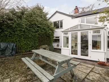 A wooden picnic table on a stone patio outside a white house with a conservatory at Pippins in Bream