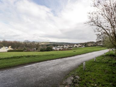 A paved road with grass fields and houses in the background at Pippins in Bream