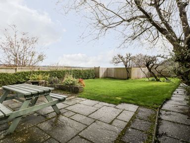 A backyard with a wooden picnic table on a stone patio a grassy lawn trees and a wooden fence at Pippins in Bream
