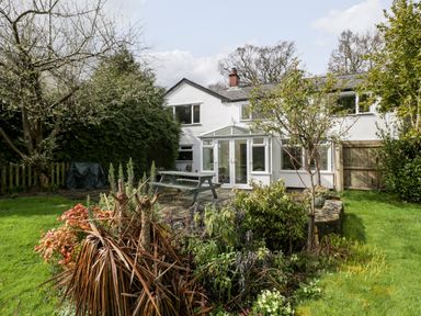 A garden with a patio table and plants in front of a white house with a conservatory at Pippins in Bream