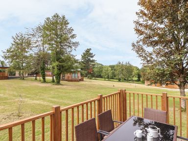 An outdoor patio with a table and chairs overlooking a grassy area with trees and wooden cabins at Ash in Truro