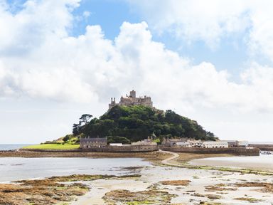 A castle on a hill surrounded by greenery and stone buildings near a rocky shoreline at Ash in Truro
