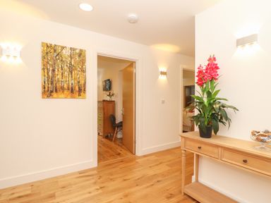 A hallway with wooden floor a wooden console table with a pink flower plant and a painting of trees on the wall at Ash in Truro