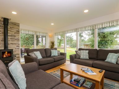 A living room with three brown sofas around a wooden coffee table with board games and books and a fireplace at Ash in Truro