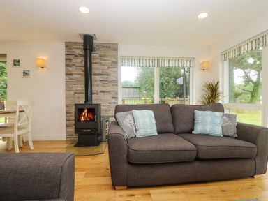 A living room with a wood-burning stove beside a gray sofa with cushions and windows overlooking a garden at Ash in Truro