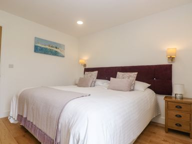 A bedroom with a double bed with purple headboard and pillows a wooden nightstand with lamp and wall lights at Ash in Truro