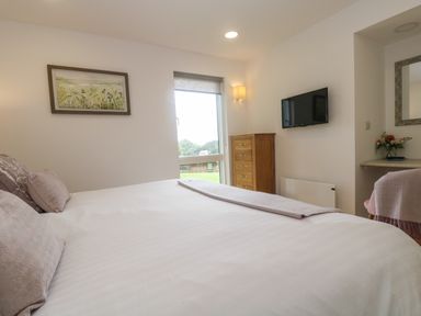 A bedroom with a bed pillows wall art a dresser a wall mounted tv and a chair at Ash in Truro