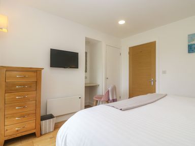 A bedroom with a bed a wooden chest of drawers a wall-mounted television and a pink chair at Ash in Truro