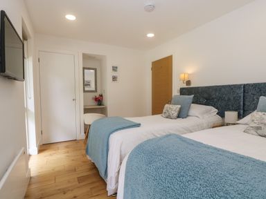 A bedroom with two single beds blue blankets a wall-mounted tv and a small desk with a chair at Ash in Truro