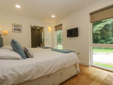 A bedroom with twin beds a wall-mounted tv large windows and a bathroom door at Ash in Truro