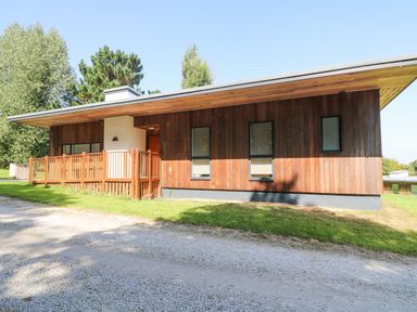 A single-story wooden house with a fenced porch and gravel driveway surrounded by grass at Ash in Truro