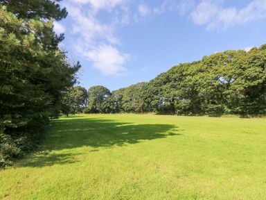 A grassy field with trees along the edges under a partly cloudy sky at Ash in Truro