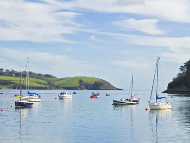 Boats floating on calm water with green hills and trees in the background at Long House Boskensoe Barns in Mawnan Smith