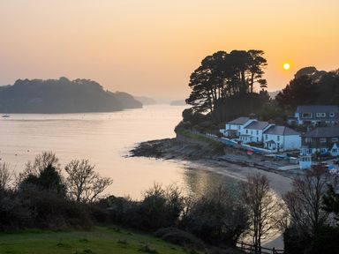 A coastal scene with houses near a beach and trees at sunset at Long House Boskensoe Barns in Mawnan Smith