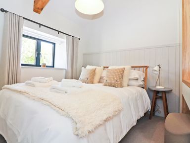 A bedroom with a bed with pillows and towels next to a window and bedside table with lamp at Long House Boskensoe Barns in Mawnan Smith