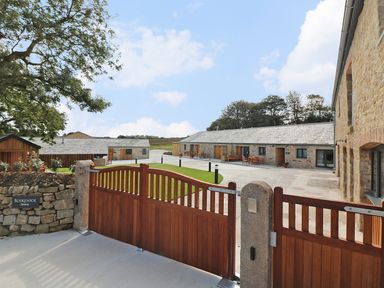 An entrance gate opening to a courtyard with stone buildings and outdoor seating at Long House Boskensoe Barns in Mawnan Smith