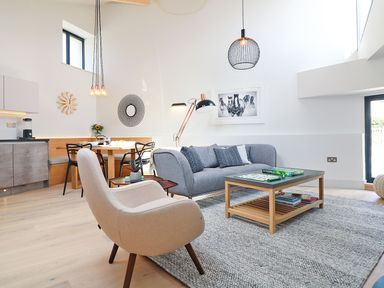 A living room with a beige armchair a gray sofa and a wooden coffee table with a scrabble game at Long House Boskensoe Barns Mawnan Smith