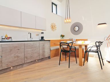 A kitchen and dining area with a wooden table black chairs a built-in bench and modern cabinets at Long House Boskensoe Barns in Mawnan Smith