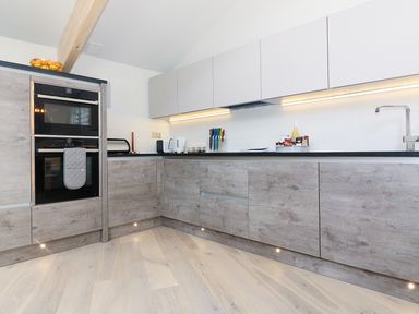 A kitchen with wooden cabinets a built in oven a countertop with a toaster knives and a sink at Long House Boskensoe Barns in Mawnan Smith