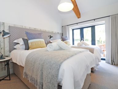 A bedroom with two beds blankets pillows and lamps at Long House Boskensoe Barns in Mawnan Smith