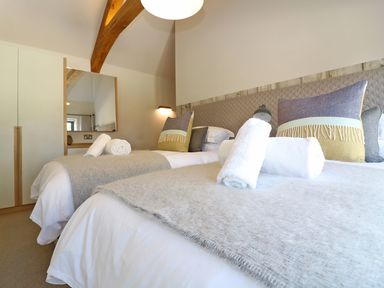 A bedroom with two single beds white bedding rolled towels and cushions at Long House Boskensoe Barns in Mawnan Smith