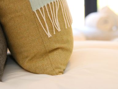 A close up of a yellow cushion with a fringe throw on a white bed at Long House Boskensoe Barns in Mawnan Smith