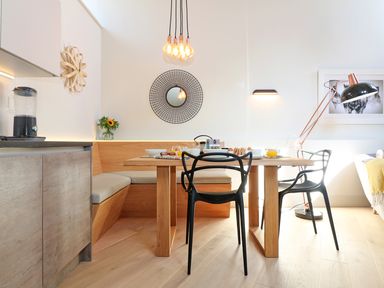 A dining area with a wooden table black chairs and a corner bench with cushions in a kitchen at Long House Boskensoe Barns in Mawnan Smith