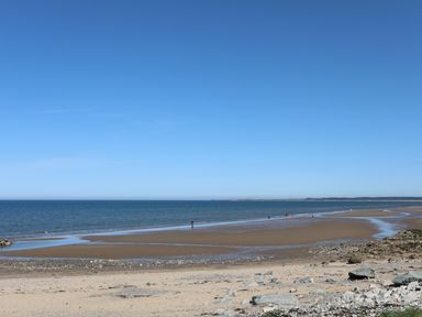 A beach with sand rocks and people walking near the shoreline at Sea Spray in Dinas Dinlle