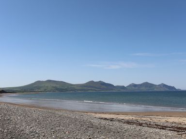 A rocky beach with a view of mountains and the sea under a clear sky at Sea Spray in Dinas Dinlle