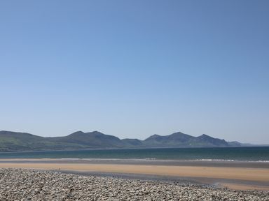 A pebble beach with a sandy shore and sea in front of distant mountains at Sea Spray in Dinas Dinlle