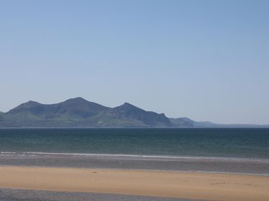 A sandy beach with calm sea water and mountains in the distance at Sea Spray in Dinas Dinlle