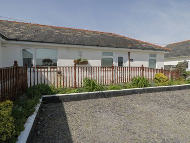 A single story house with a wooden railing and garden in front at Sea Spray in Dinas Dinlle